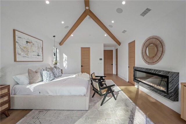 bedroom featuring vaulted ceiling with beams and light hardwood / wood-style flooring