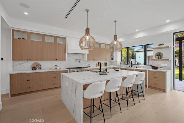 kitchen featuring backsplash, a kitchen island with sink, sink, light wood-type flooring, and a kitchen bar