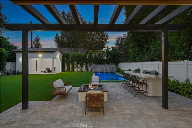 patio terrace at dusk featuring a fire pit, a fenced in pool, an outdoor bar, pool water feature, and a yard