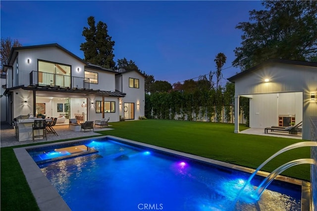 back of house featuring a lawn, a pool with hot tub, a balcony, and a patio