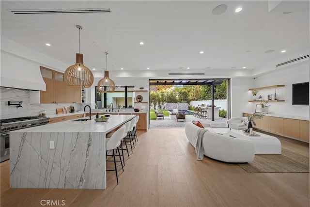 kitchen featuring light stone countertops, sink, a large island, light hardwood / wood-style flooring, and stainless steel stove