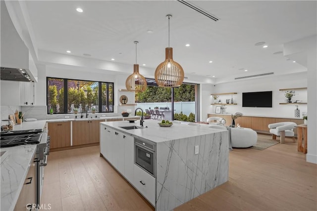 kitchen featuring light stone counters, white cabinets, light hardwood / wood-style floors, hanging light fixtures, and an island with sink