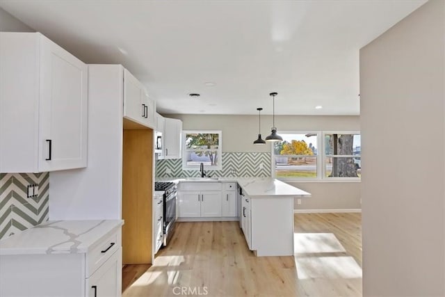 kitchen with kitchen peninsula, decorative light fixtures, light hardwood / wood-style floors, white cabinetry, and stainless steel appliances