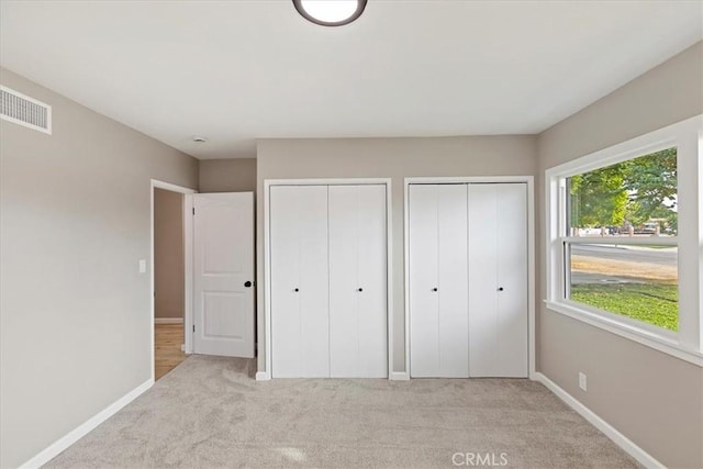 unfurnished bedroom featuring light carpet and two closets