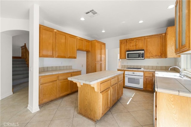 kitchen with tile counters, a center island, light tile patterned flooring, and white appliances