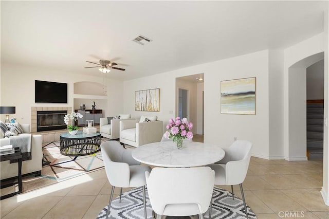 tiled dining area featuring a tile fireplace, built in shelves, and ceiling fan