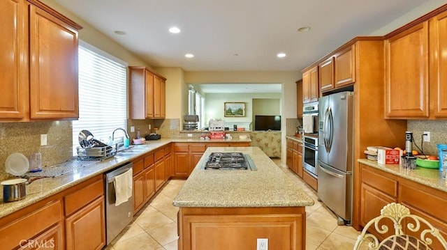 kitchen with sink, light stone counters, backsplash, a kitchen island, and appliances with stainless steel finishes