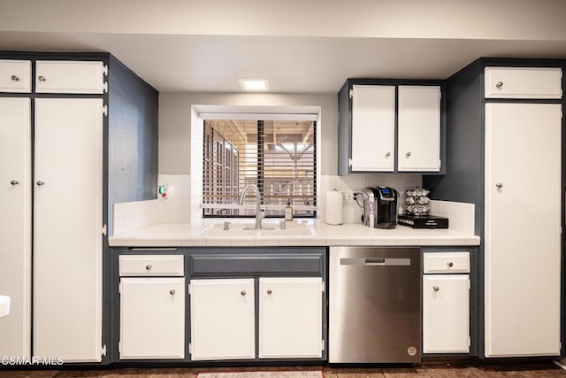 kitchen featuring tile countertops, backsplash, sink, stainless steel dishwasher, and white cabinetry