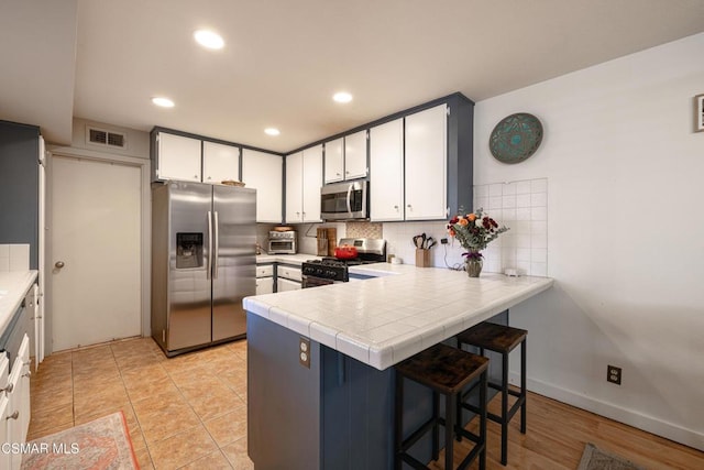 kitchen with white cabinetry, tile counters, a kitchen bar, decorative backsplash, and appliances with stainless steel finishes