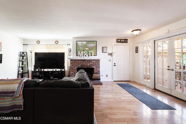 living room with a brick fireplace, french doors, a textured ceiling, and light hardwood / wood-style flooring