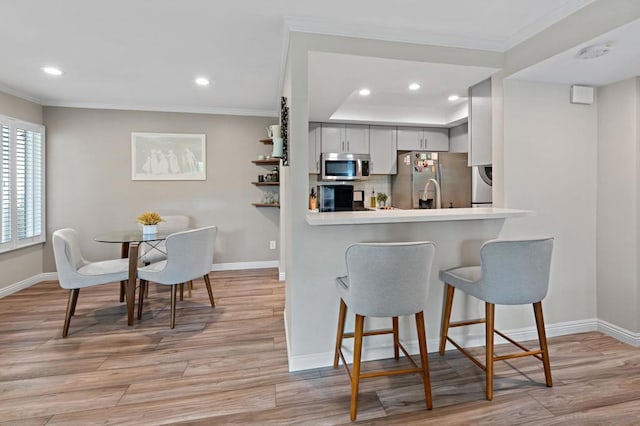 kitchen with gray cabinetry, light wood-type flooring, kitchen peninsula, and appliances with stainless steel finishes