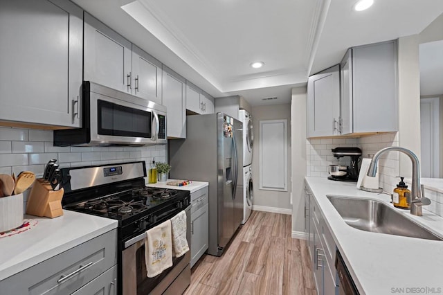 kitchen featuring sink, stacked washer and dryer, decorative backsplash, light hardwood / wood-style floors, and stainless steel appliances