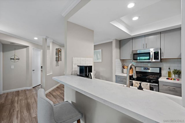 kitchen featuring appliances with stainless steel finishes, tasteful backsplash, crown molding, light hardwood / wood-style flooring, and gray cabinets