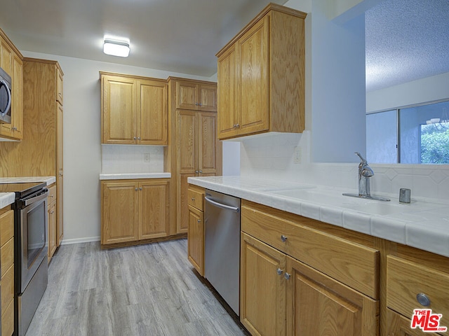 kitchen featuring light wood-type flooring, tasteful backsplash, stainless steel appliances, sink, and tile counters