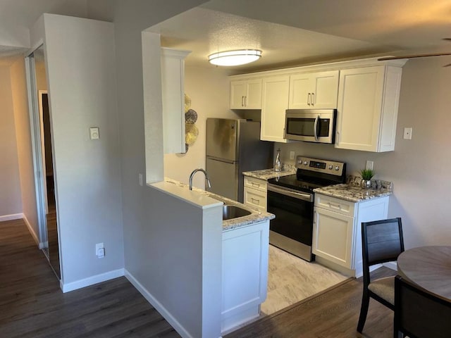 kitchen with light stone countertops, white cabinetry, appliances with stainless steel finishes, and light wood-type flooring