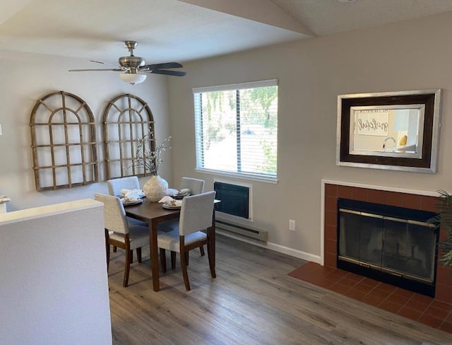 dining room featuring ceiling fan, dark hardwood / wood-style flooring, a tiled fireplace, and a baseboard heating unit