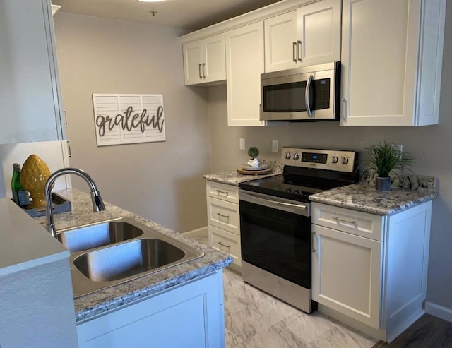 kitchen with light stone countertops, appliances with stainless steel finishes, sink, and white cabinets