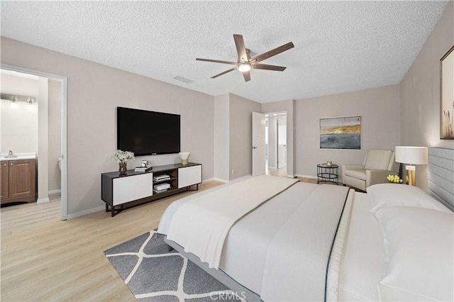 bedroom featuring ceiling fan, light hardwood / wood-style flooring, ensuite bathroom, and a textured ceiling