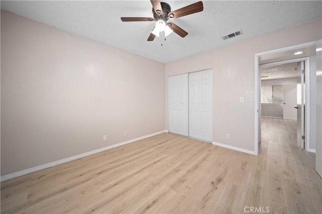 unfurnished bedroom featuring a closet, a textured ceiling, light hardwood / wood-style floors, and ceiling fan