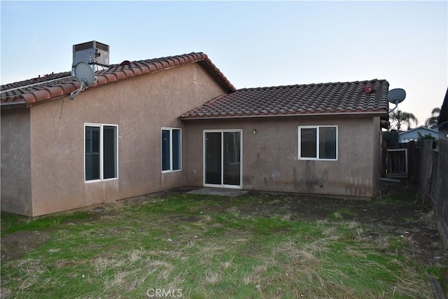 rear view of property featuring a tiled roof, a yard, fence, and stucco siding