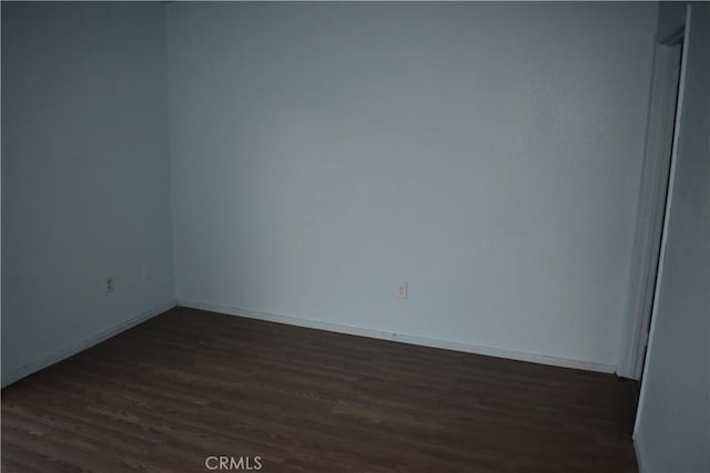 spare room with baseboards and dark wood-style flooring