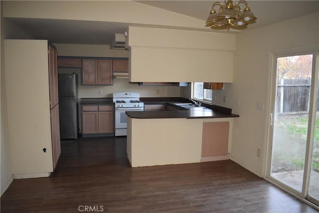 kitchen featuring a peninsula, freestanding refrigerator, a sink, dark countertops, and white gas range