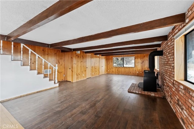 unfurnished living room featuring a wood stove, wood walls, dark wood-type flooring, and a textured ceiling