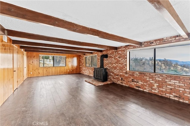 unfurnished living room featuring a mountain view, a wood stove, wooden walls, dark hardwood / wood-style flooring, and brick wall