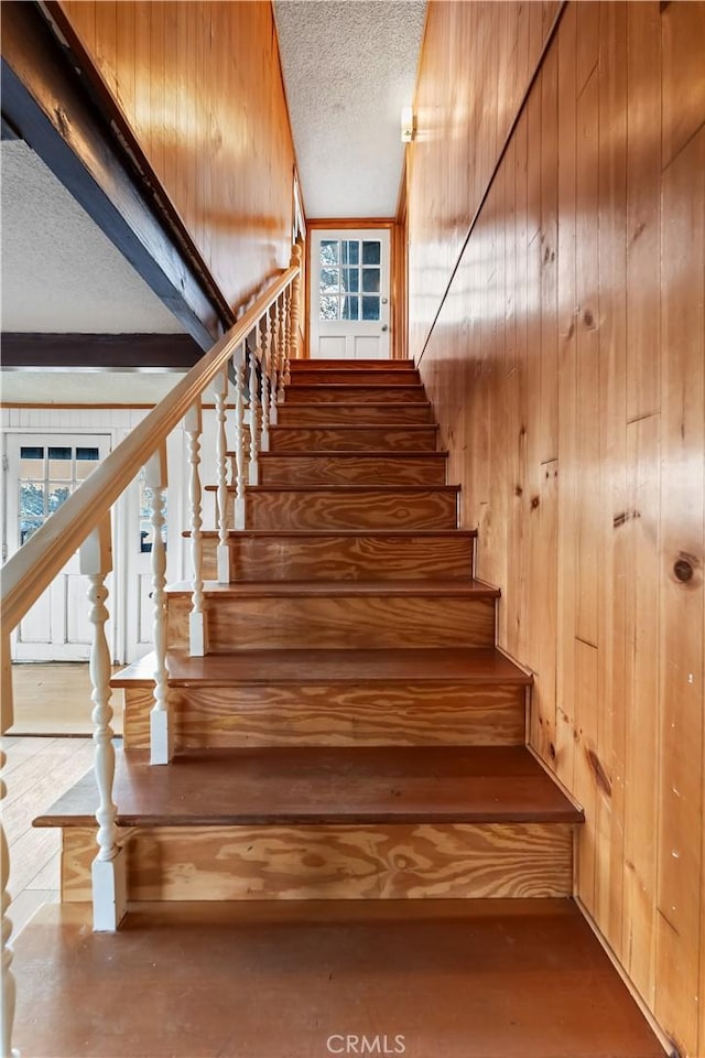 stairway featuring wooden walls, a textured ceiling, and a wealth of natural light