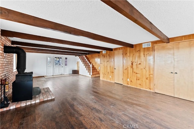 unfurnished living room with beam ceiling, a wood stove, wood walls, hardwood / wood-style floors, and a textured ceiling