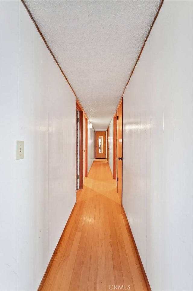 corridor with a textured ceiling and light wood-type flooring