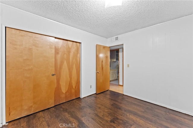 unfurnished bedroom featuring a textured ceiling, dark hardwood / wood-style floors, and a closet