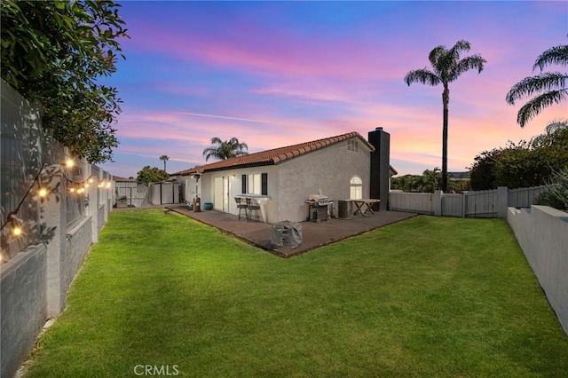 back house at dusk with a yard and a patio