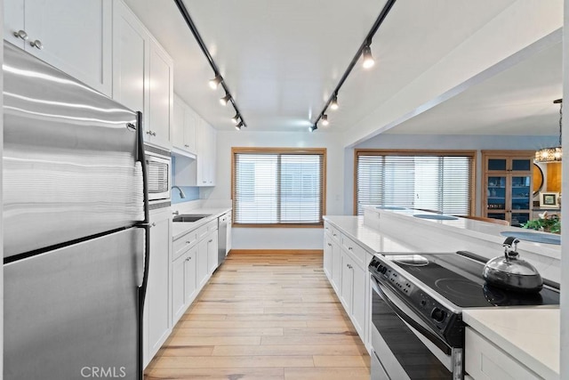 kitchen with light hardwood / wood-style floors, stainless steel appliances, pendant lighting, white cabinets, and sink