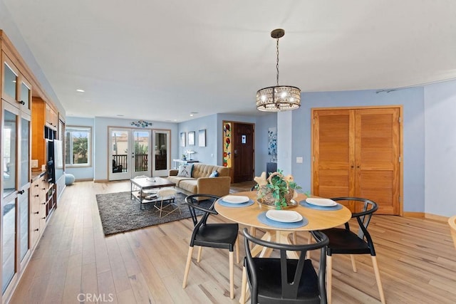 dining area with light hardwood / wood-style floors, a notable chandelier, and french doors