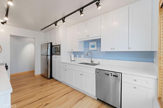 kitchen with white cabinets, appliances with stainless steel finishes, sink, and light hardwood / wood-style flooring