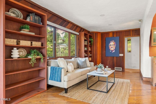 living area with ornamental molding, visible vents, wood walls, and light wood-style flooring