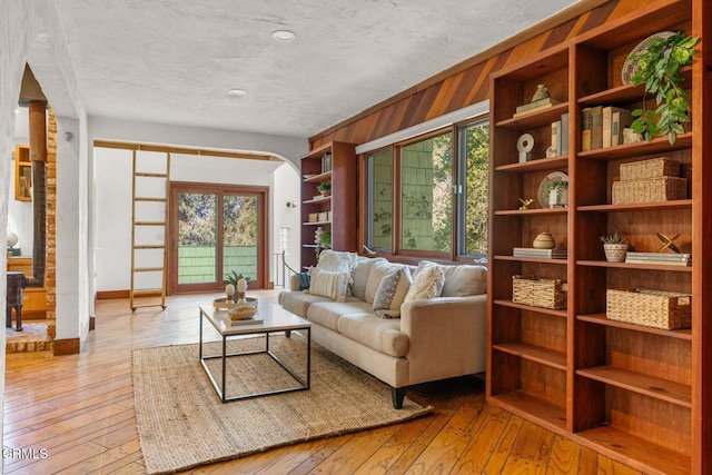 living area featuring a healthy amount of sunlight, light wood-style floors, wooden walls, and arched walkways