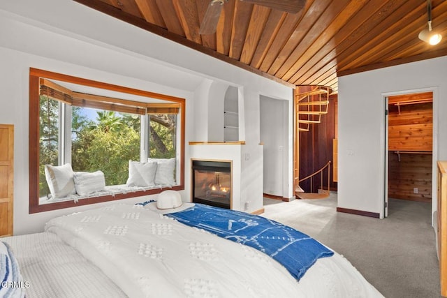 bedroom featuring wood ceiling, baseboards, a walk in closet, and a glass covered fireplace