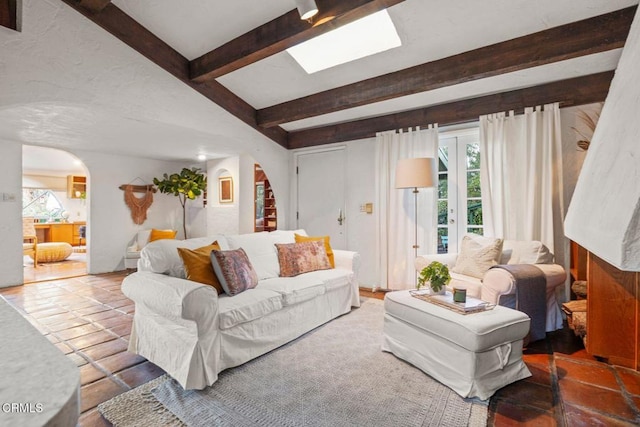 living area with arched walkways, beamed ceiling, and a skylight