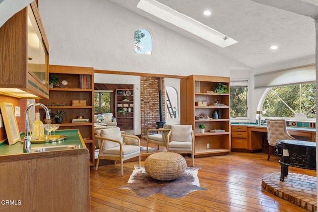 living area featuring a wood stove, a skylight, high vaulted ceiling, and hardwood / wood-style floors