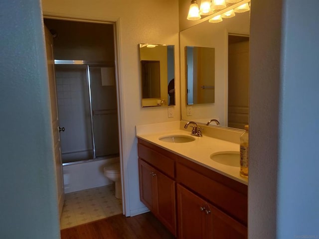 full bathroom featuring vanity, hardwood / wood-style flooring, toilet, and bath / shower combo with glass door