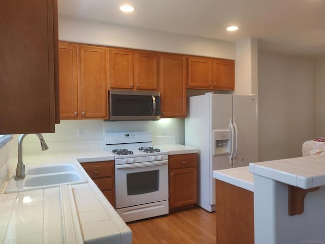 kitchen featuring tile countertops, sink, light hardwood / wood-style floors, and white appliances