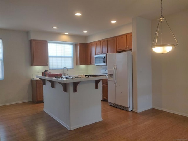 kitchen with pendant lighting, a breakfast bar, white refrigerator with ice dispenser, and light hardwood / wood-style flooring