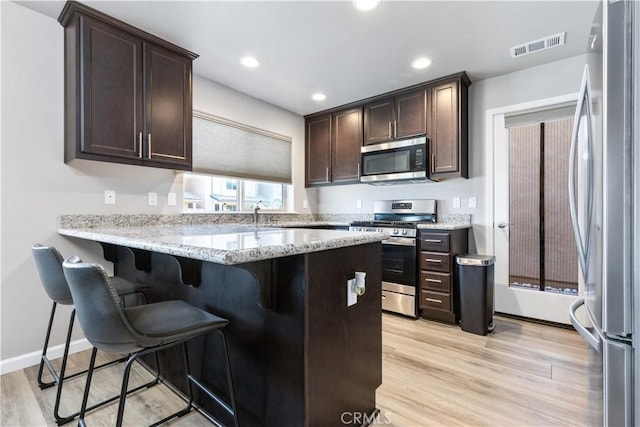 kitchen featuring a kitchen bar, appliances with stainless steel finishes, light stone countertops, and light hardwood / wood-style flooring