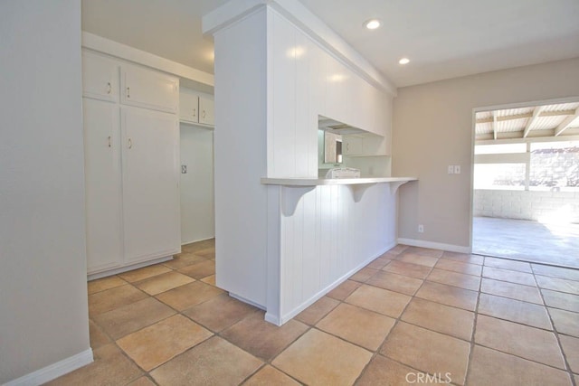 kitchen featuring kitchen peninsula, a kitchen breakfast bar, light tile patterned floors, and white cabinetry