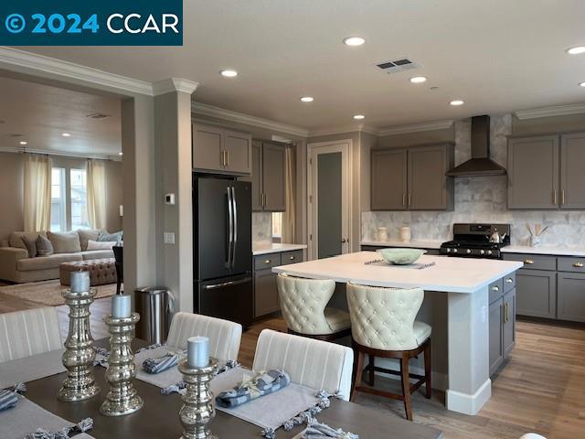 kitchen featuring refrigerator, wall chimney exhaust hood, a breakfast bar, gas stove, and a center island