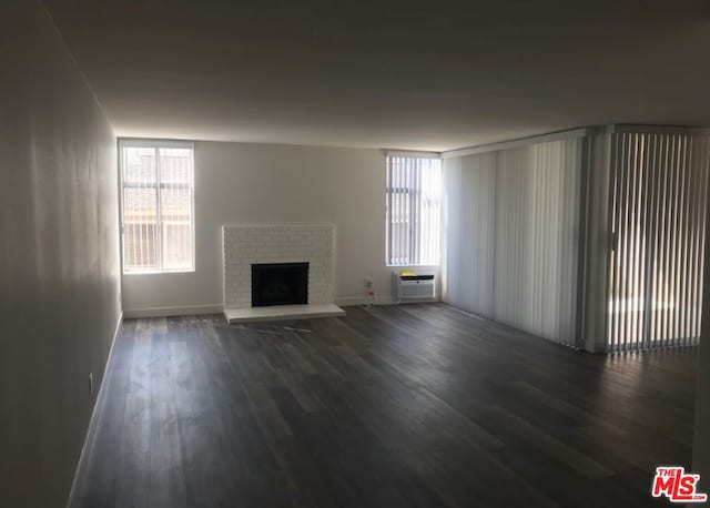 unfurnished living room with a wall mounted air conditioner, dark hardwood / wood-style flooring, and a fireplace