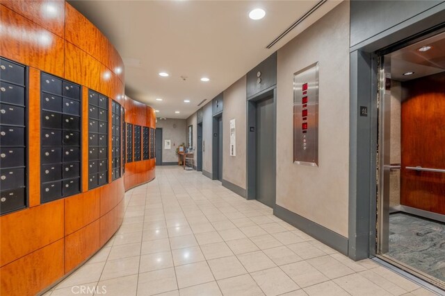 hallway featuring elevator, light tile patterned flooring, and a mail area