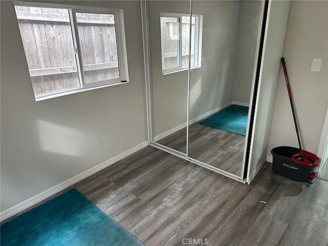 unfurnished bedroom with multiple windows, a closet, and dark wood-type flooring